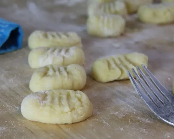 Frisch geformte Gnocchi liegen auf bemehltem Holz. Eine Gabel und ein blauer Lappen deuten auf die Zubereitung von Gnocchi Rezepten hin.