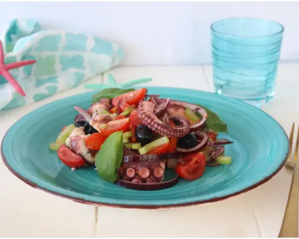Un invitante polpo alla catalana su un piatto turchese, con pomodorini, olive e basilico. Fresco e saporito.