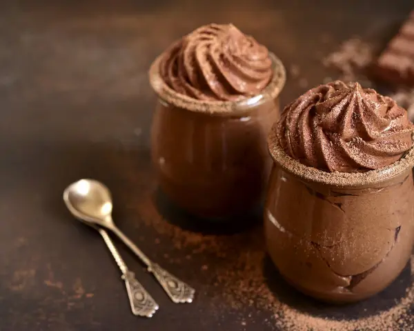 Deux pots de mousse au chocolat onctueuse, saupoudrés de cacao, avec deux cuillères argentées.