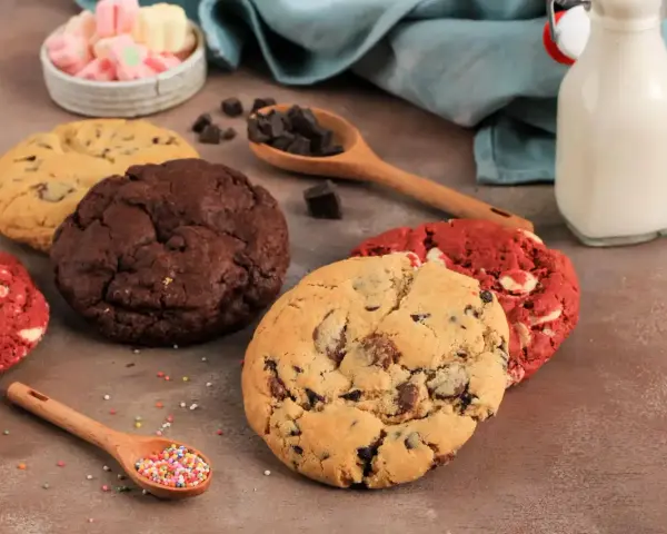 Verschiedene amerikanische Cookies: Schoko, Red Velvet und Chocolate Chip. Dazu Marshmallows, Schokostückchen und Milch.