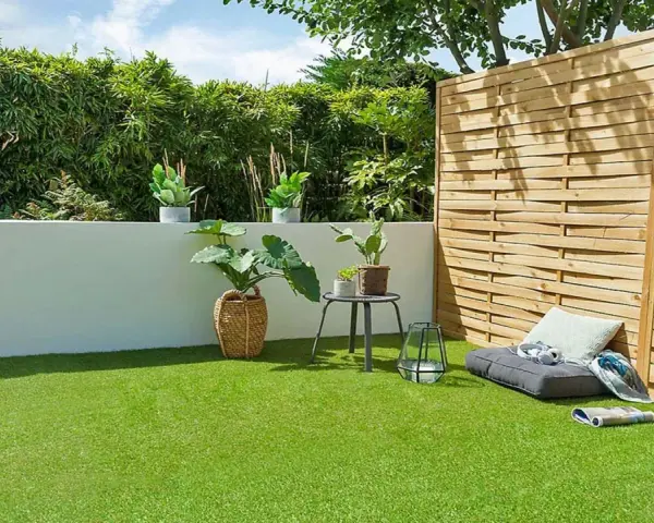 Terraza con césped artificial verde vibrante, plantas en macetas, un banco y una valla de madera.
