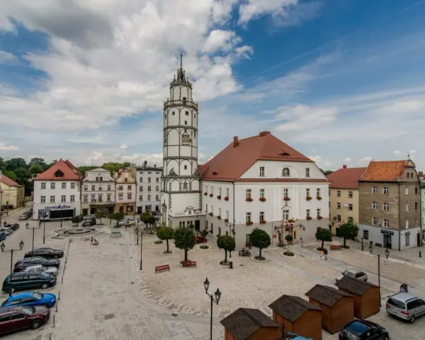 Rynek w Paczkowie, polskie Carcassonne, z ratuszem i wieżą. Brukowany plac, samochody, ławki i małe drewniane budki.