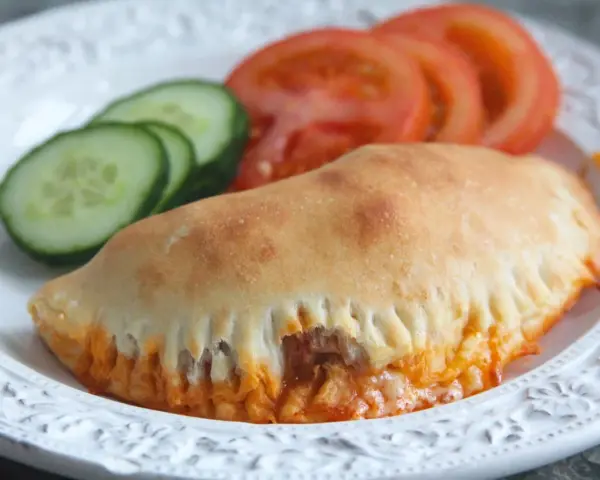En gyllene pirog med ost och tomatsås, serverad med gurka och tomat. Ett perfekt piroger recept för en snabb måltid.