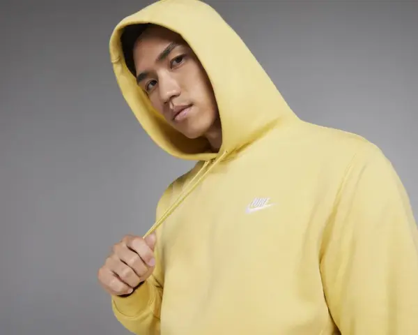 Młody mężczyzna w żółtej bluzie z kapturem Nike Club.