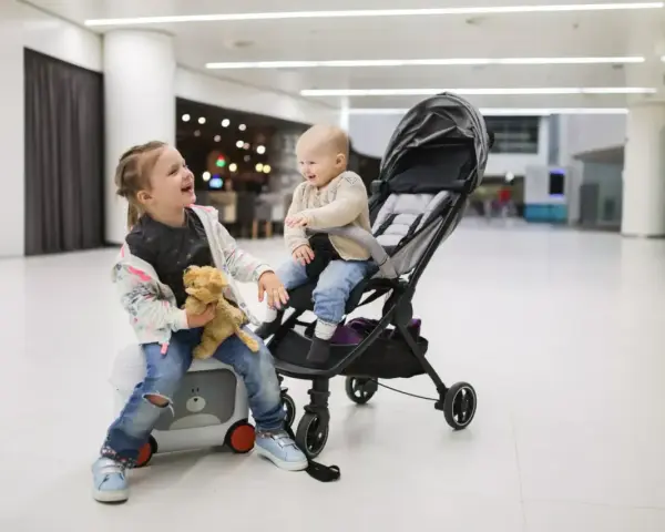Dzieci w podróży z Ryanair. Starsza siostra siedzi na walizce z misiem, młodsza w wózku.