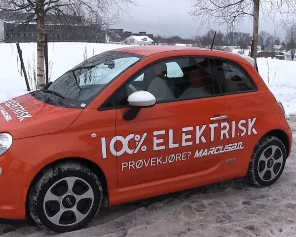 Pomarańczowy Fiat 500e w zimowej scenerii, z napisem "100% ELEKTRISK". Sprawdź zasięg tego elektryka!