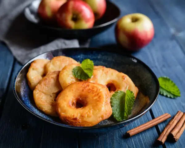 Délicieux beignets aux pommes dorés, garnis de menthe fraîche et accompagnés de bâtons de cannelle sur une table en bois bleu.