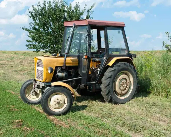 Żółty Ursus C-360 na łące. Pytanie o to, ile oleju do filtra powietrza C-360, jest kluczowe dla jego sprawnej pracy.