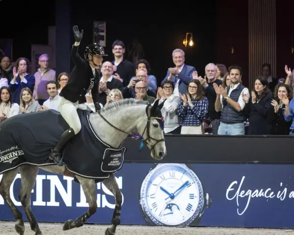 Cavalier(e) saluant la foule, son cheval gris couvert d'une cape aux couleurs de la Longines FEI Jumping World Cup.