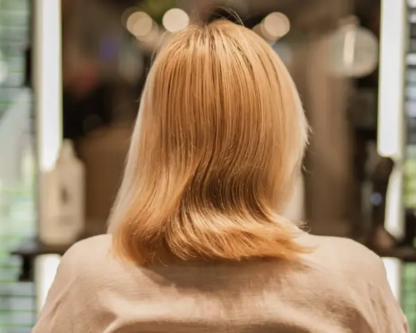 Kobieta z blond włosami, zastanawia się, jak nosić siwe włosy. Włosy są średniej długości, lekko falowane.