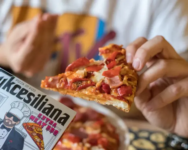 Kawałek pysznej pizzy od Kizo, z dodatkami mięsnymi i papryką, na opakowaniu widnieje napis "Sukcesiliana Extra Meat BBQ".