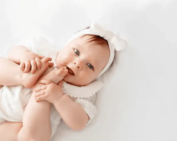 La bebé Cora, con su diadema de lazo blanco, juega con sus pies.