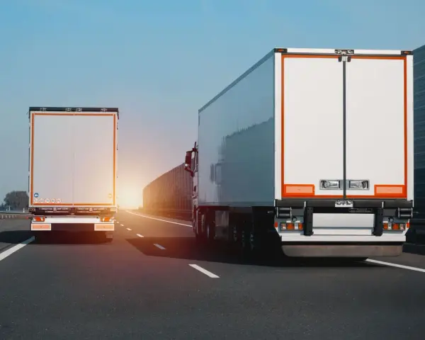 Dwa białe tiry jadą autostradą. Na jednym z nich widać znak zakazu wyprzedzania dla ciężarówek.