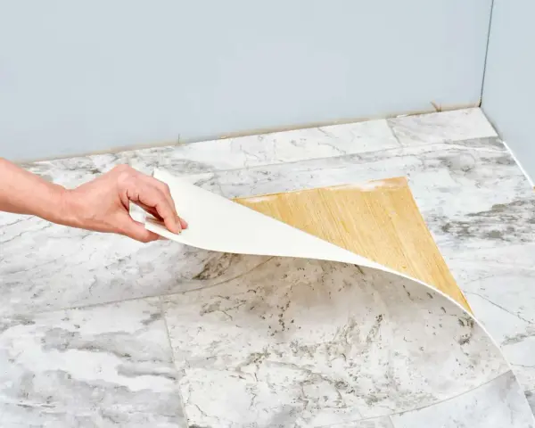 Mano retirando capa de vinilo del suelo. Un paso clave para saber como quitar pintura de caucho del suelo.