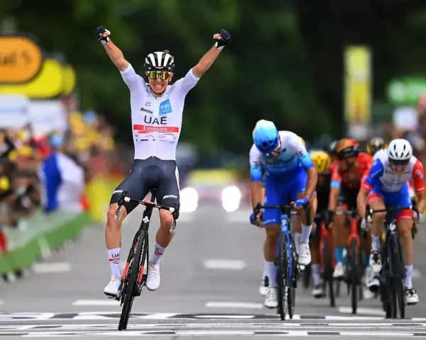 A cyclist in a white UAE Emirates jersey celebrates victory at the Tour de France, arms raised in triumph as he crosses the finish line.