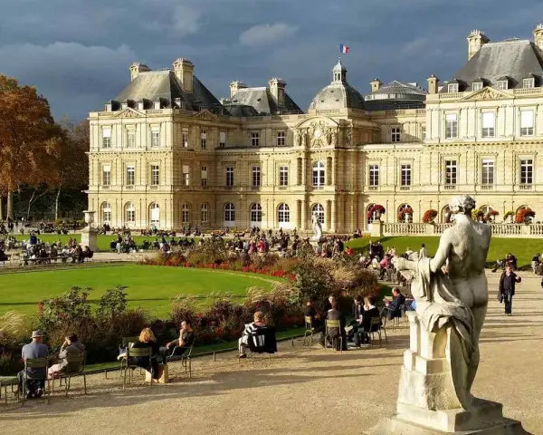 Palacio de Luxemburgo y su jardín con gente sentada y un monumento.