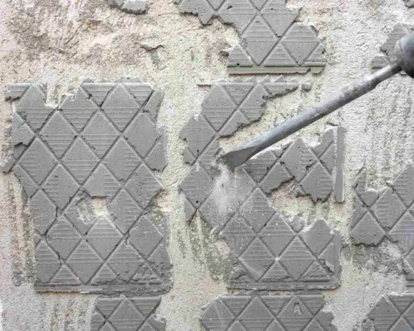 Outil pneumatique en action pour enlever ciment colle sur carrelage. Poussière et débris volent.