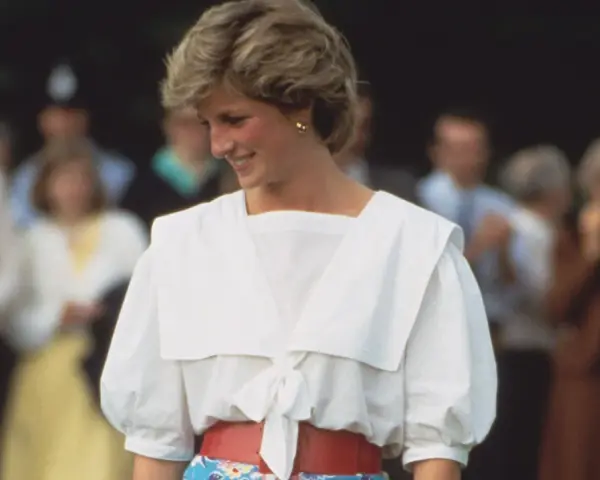 Lady Di sonríe con un conjunto blanco y rojo, un ejemplo de sus icónicos outfits.