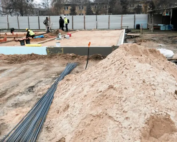Budowa w marcu 2026. Działka z uregulowanym stanem prawnym, przygotowana pod fundamenty. Piasek, zbrojenie i pracownicy na placu budowy.
