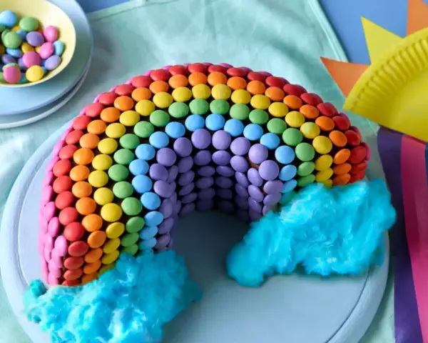 Bunter regenbogen kuchen, verziert mit vielen bunten Smarties und blauer Zuckerwatte als Wolken. Ein Fest für die Augen!