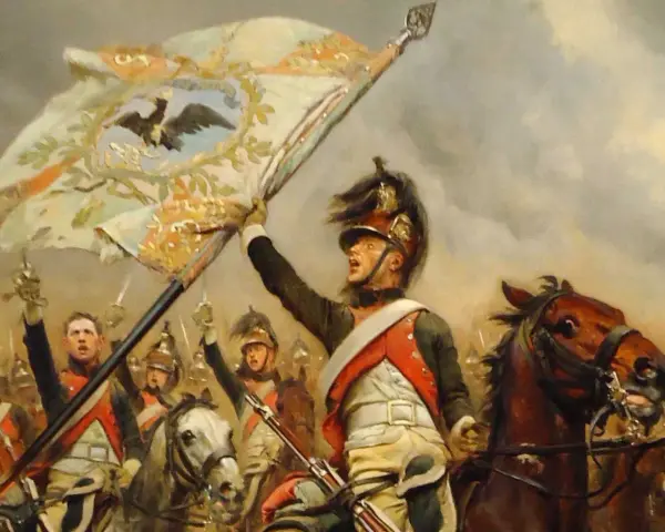 Un porte-étendard, au cœur des 10 batailles de Napoléon, brandit fièrement l'aigle impérial. Cavaliers et chevaux chargent.