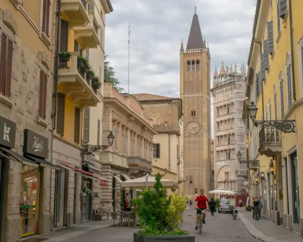 A man cycles down a street in Parma, Italy, with a tall clock tower in the background. This view captures the essence of a journey from Bologna to Parma.