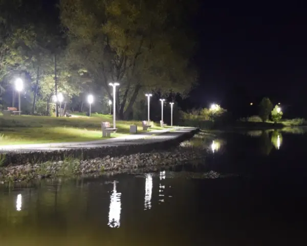 Nocny spacer nad zalewem Wolbromskim. Latarnie oświetlają ścieżkę i ławki, odbijając się w spokojnej tafli wody.