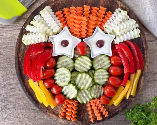 Eine bunte Rohkostplatte für Kinder, gestaltet als lustige Eule mit Sternen als Augen und verschiedenen Gemüsesorten.