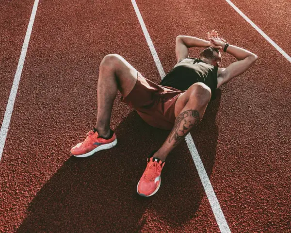 Atleta esausto sdraiato su una pista da corsa, con le mani sulla testa, forse vittima della sindrome da overtraining.