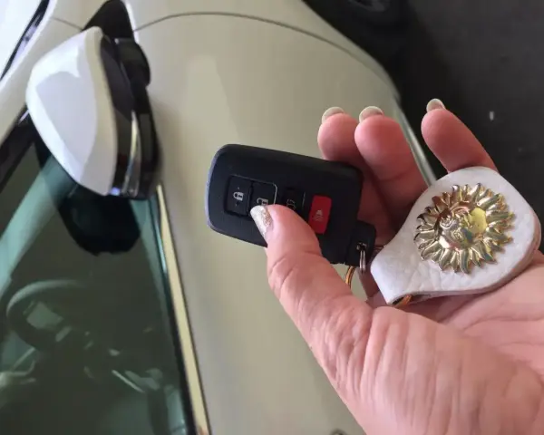 Dłoń trzyma kluczyk samochodowy z breloczkiem w kształcie słońca. Kluczyk z przyciskami blokady i alarmu to część systemu, który chroni auto, czyli co to jest immobilizer.
