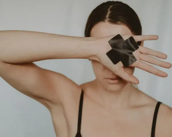 Kobieta zakrywa oczy dłonią z czarną taśmą w kształcie krzyża, symbolizującą trauma seksualna i potrzebę uzdrowienia.