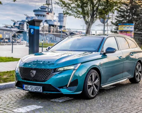 Turkusowe kombi Peugeot 308 zaparkowane na bruku, w tle okręt wojenny.