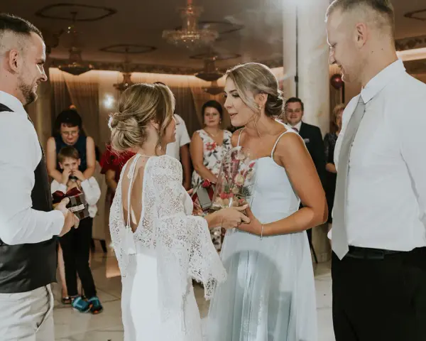 Nietypowe podziękowania dla rodziców na weselu: panna młoda z bukietem w szkle i pan młody z prezentem.