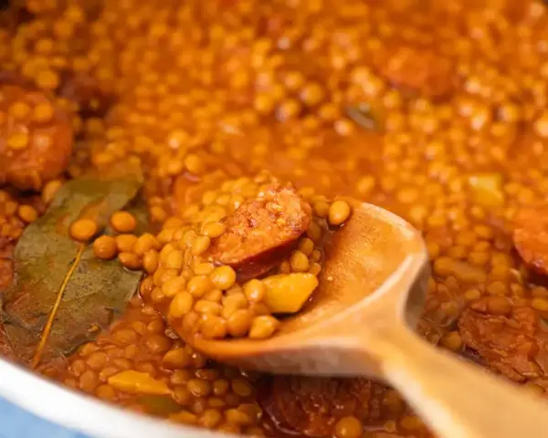 Primer plano de lentejas con chorizo y laurel en una cuchara de madera.