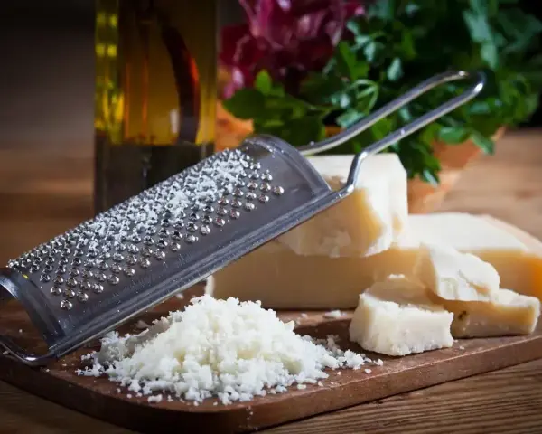 Tarka z kawałkami sera **padano ser** i świeżo startym serem. Obok butelka oliwy i zielenina.