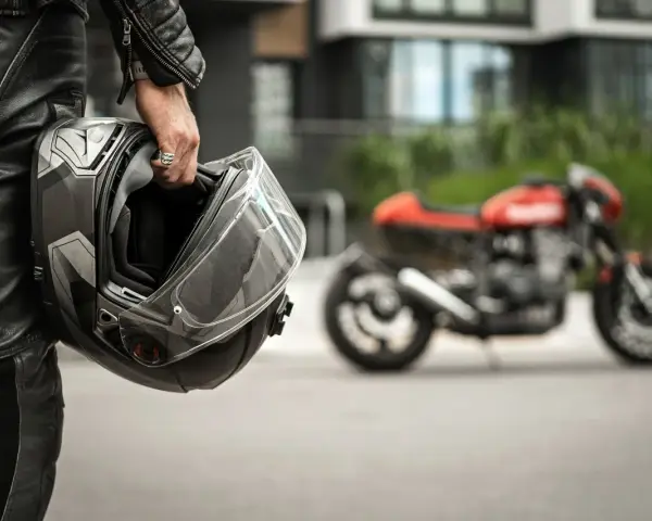 Motociclista in pelle tiene un casco, pronto per misurare la circonferenza della testa per un acquisto perfetto. Moto rossa sfocata sullo sfondo.