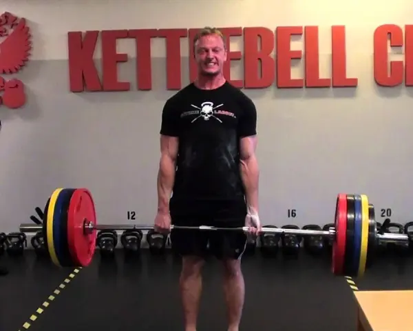 Man i gymmet förbereder sig för ett styrkelyft program. Han håller i en skivstång med vikter.
