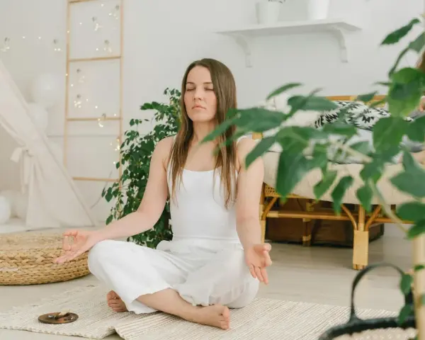 Frau in weißer Kleidung meditiert im Lotussitz. Eine sanfte Metta-Meditation-Anleitung textlich wäre hier passend.