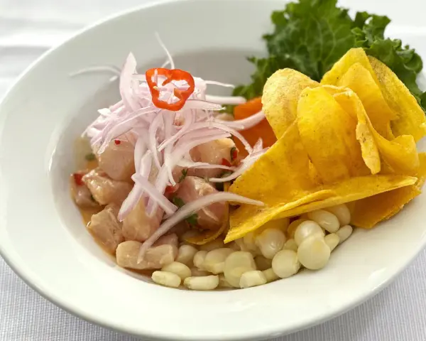 Delicioso ceviche peruano con trozos de pescado fresco, cebolla morada, chile, maíz tierno y chips de plátano.