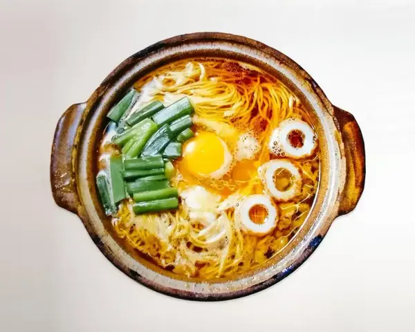 Gorący garnek z aromatycznym bulionem, żółtkiem jajka, zielonym szczypiorkiem i krążkami rybnymi. Czy to ramen czy udon?