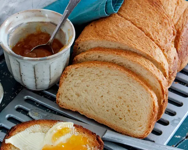 Ein Laib **sauerteig Toastbrot** ist aufgeschnitten. Daneben stehen Marmelade, Butter und ein Messer mit einem Stück Brot, das bestrichen ist.