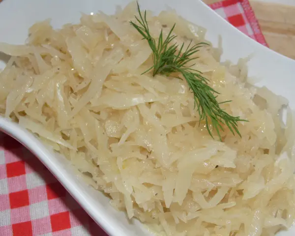 Gotowana biała kapusta do obiadu, podana w białej misce, ozdobiona gałązką koperku.