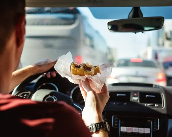 Uomo al volante mangia un panino in un ingorgo. Si può mangiare mentre si guida, ma attenzione alla sicurezza!