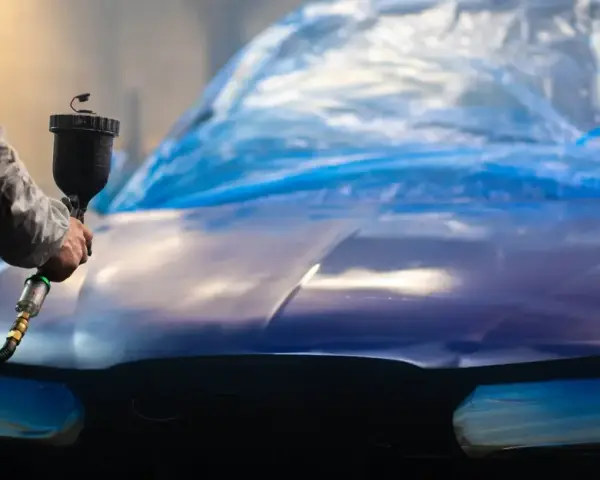Person lackar om bilen billigt med sprutpistol. Bilen är täckt med blå plast.