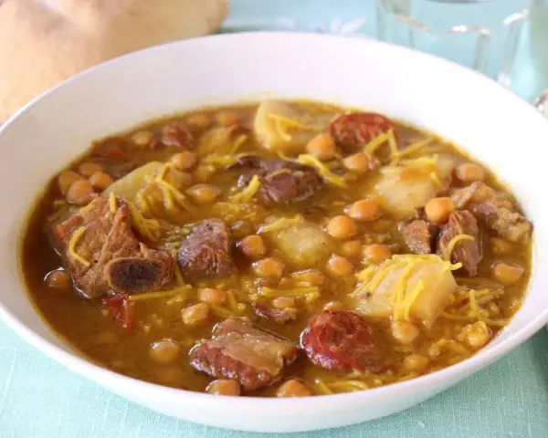 Un reconfortante rancho canario en un cuenco blanco, con garbanzos, trozos de carne, patatas y fideos finos.