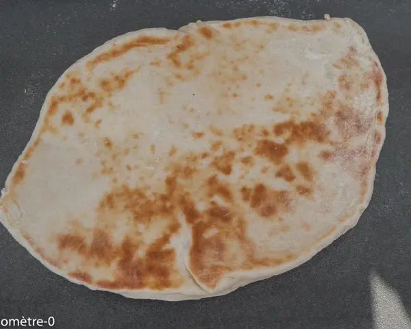 Un naan au fromage, peut-être avec un peu de La Vache qui rit, doré et moelleux, prêt à être dégusté.