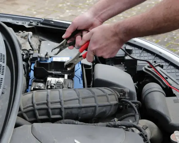 Ręce podłączają kable rozruchowe do akumulatora, bo auto nie odpala.
