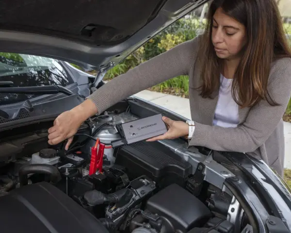 Woman connects a jump starter to a car battery. She's learning how to reset my jump starter.