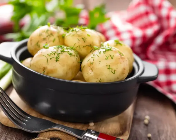 Gotujesz ziemniaki na ból ucha? Te młode ziemniaczki, posypane koperkiem, wyglądają apetycznie. Obok widelec i czerwono-biała serwetka.