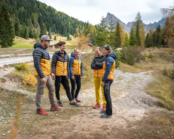 Gruppo di escursionisti con giacche imbottite gialle e blu, pantaloni tecnici e scarponi. Perfetto esempio di come vestirsi in montagna per un'avventura autunnale.